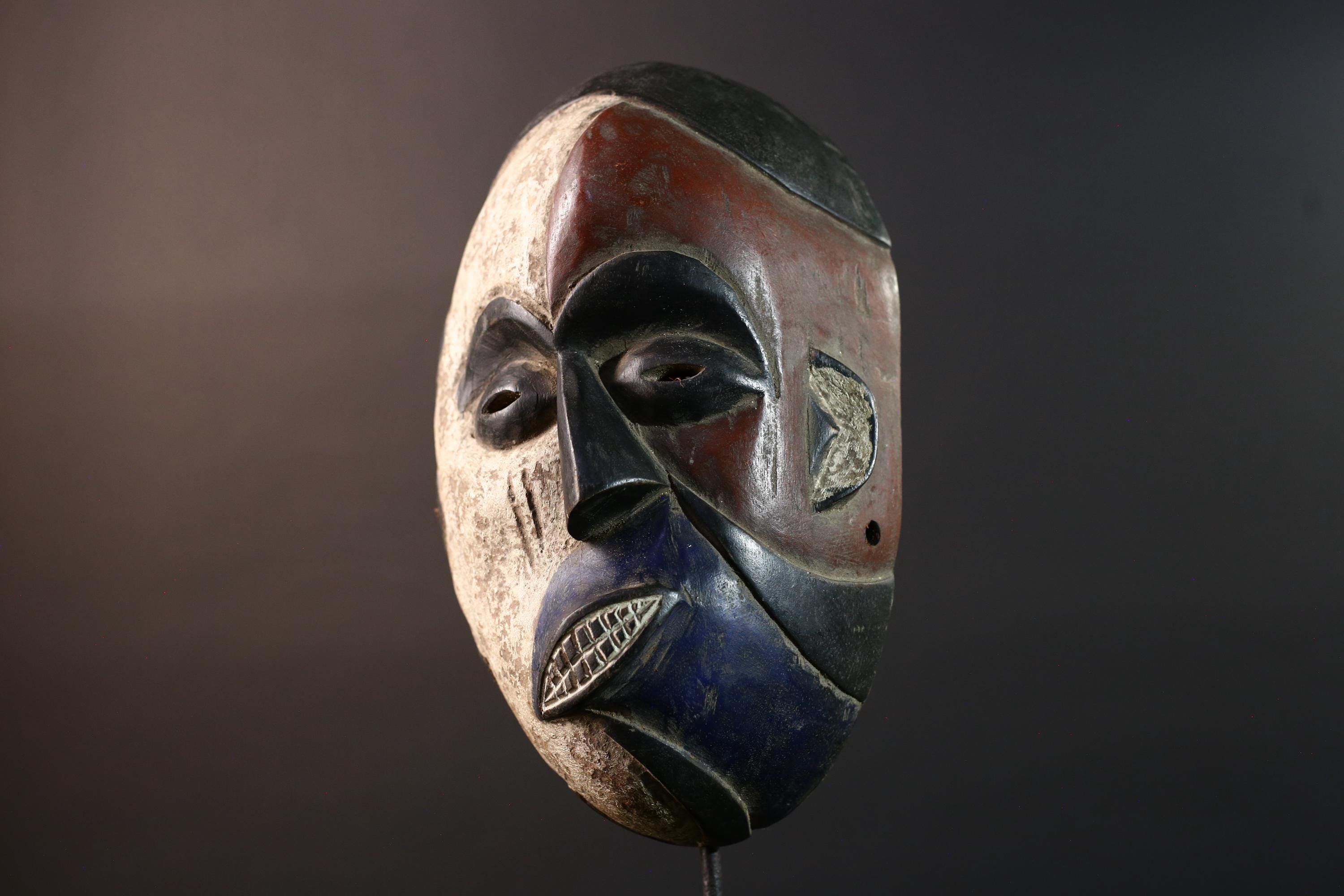 African wall decor Dan tribal mask with red white and blue split face carved features and symbolic teeth for expressive rustic display G5501